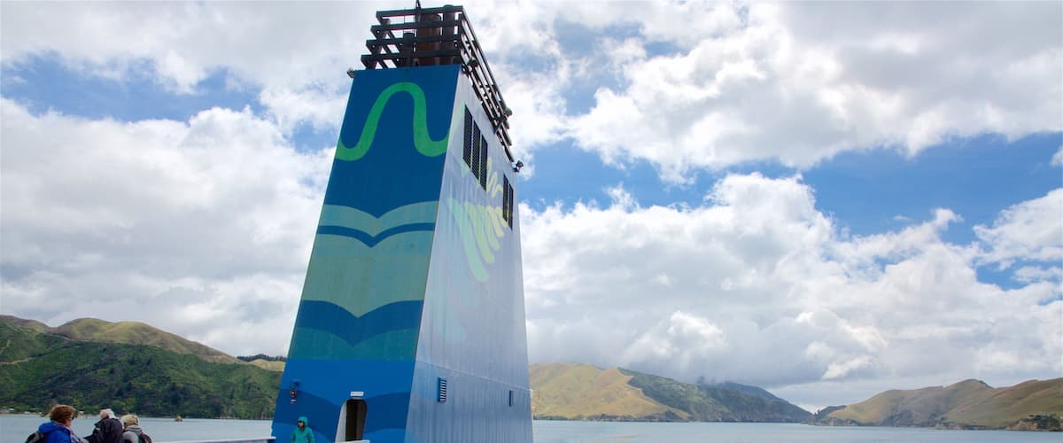 A ferry with a blue and green design, passengers on the deck, and a mountainous landscape in the background.