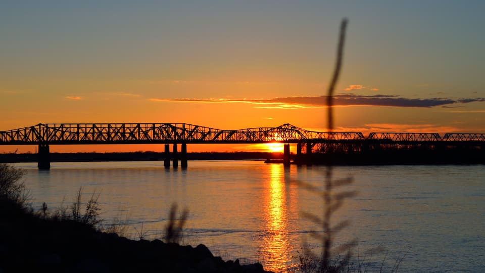 A sunset over a river with a bridge silhouetted against the sky.