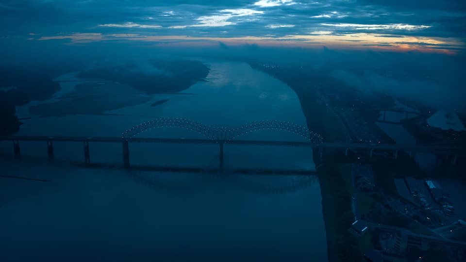 A bridge with lights, a river, and a sunset.