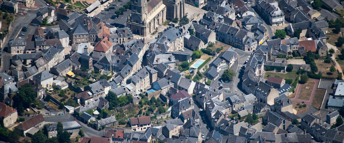 An aerial view of a historic European town with dense medieval architecture, narrow streets, and a prominent church.