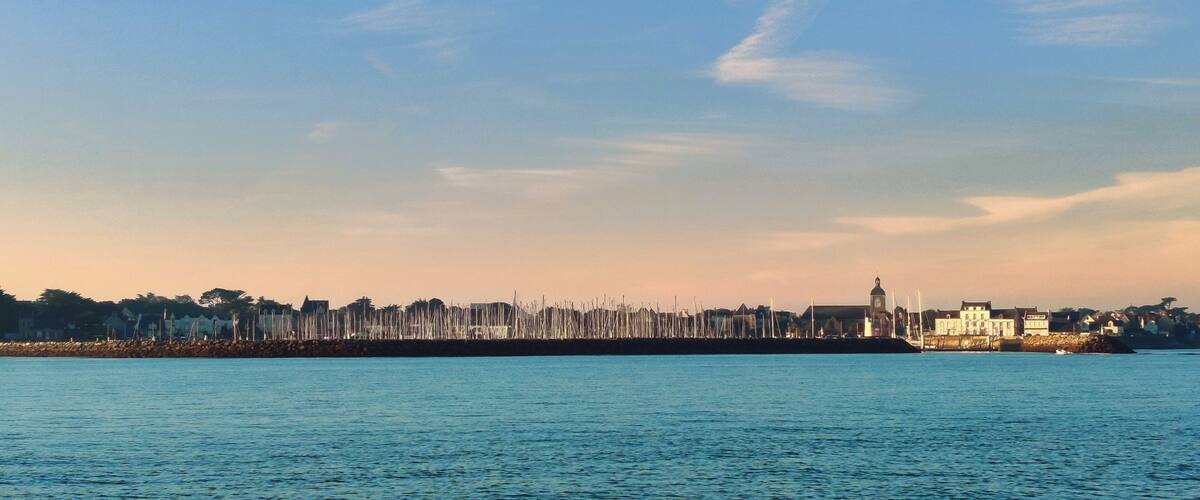 A coastal cityscape with a prominent clock tower, a breakwater, and a calm sea.