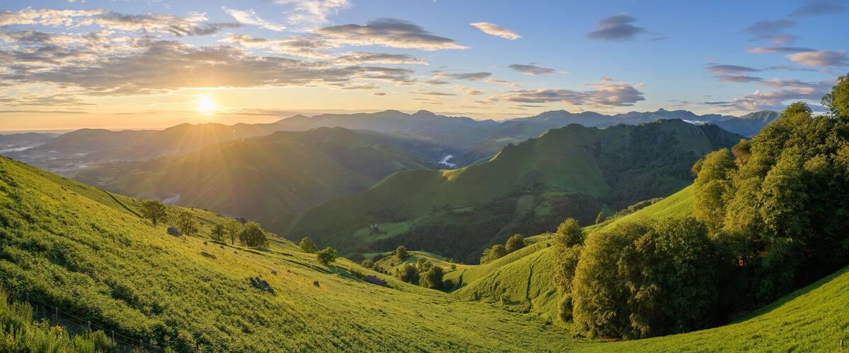 A valley with rolling hills, a river, and distant mountains under a partly cloudy sky.