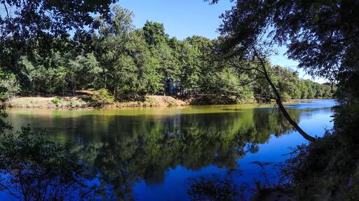 a gorgeous panoramic shot of the silky brown waters of the Chattahoochee river surrounded by lush green trees with blue sky at Jones Bridge Park Trail in Johns Creek Georgia USA