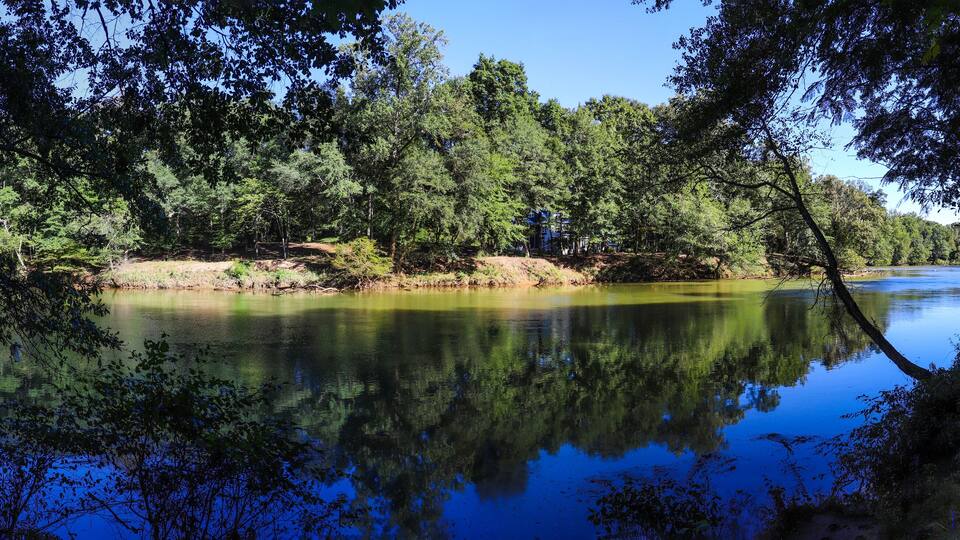 a gorgeous panoramic shot of the silky brown waters of the Chattahoochee river surrounded by lush green trees with blue sky at Jones Bridge Park Trail in Johns Creek Georgia USA