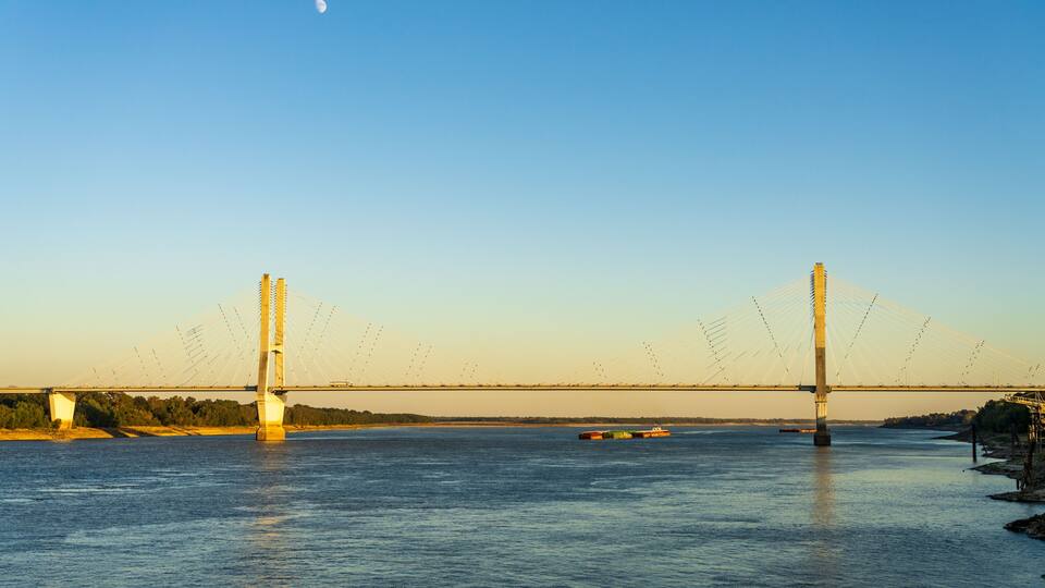 A suspension bridge over a river with a cargo ship in the water.