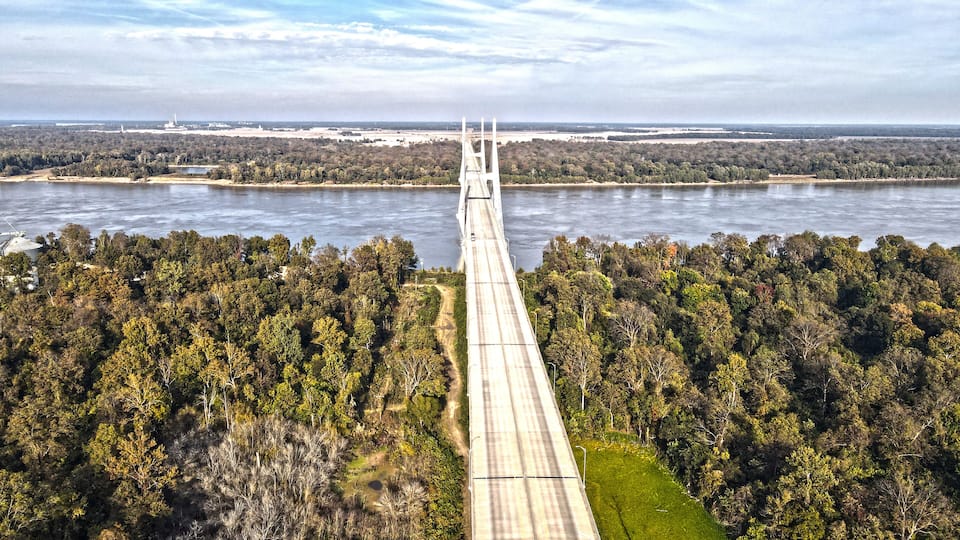 A long bridge spanning a river, surrounded by dense forest.