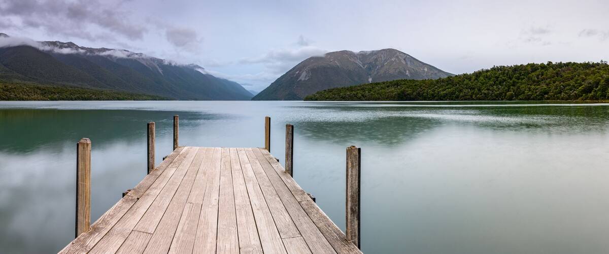 A wooden pier extending into calm waters with mountains in the background.