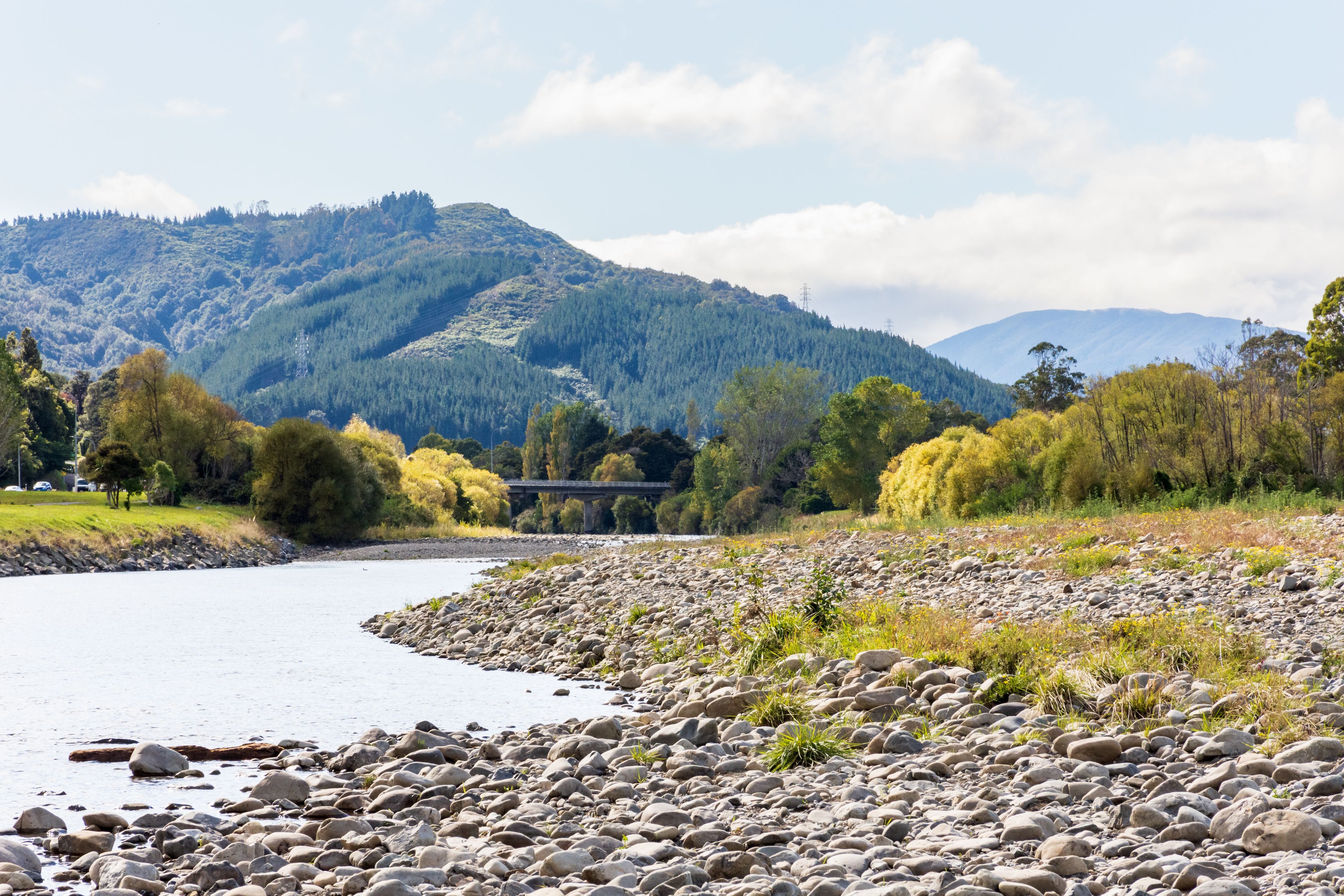 A river with a rocky shoreline, a bridge, and a mountainous backdrop.