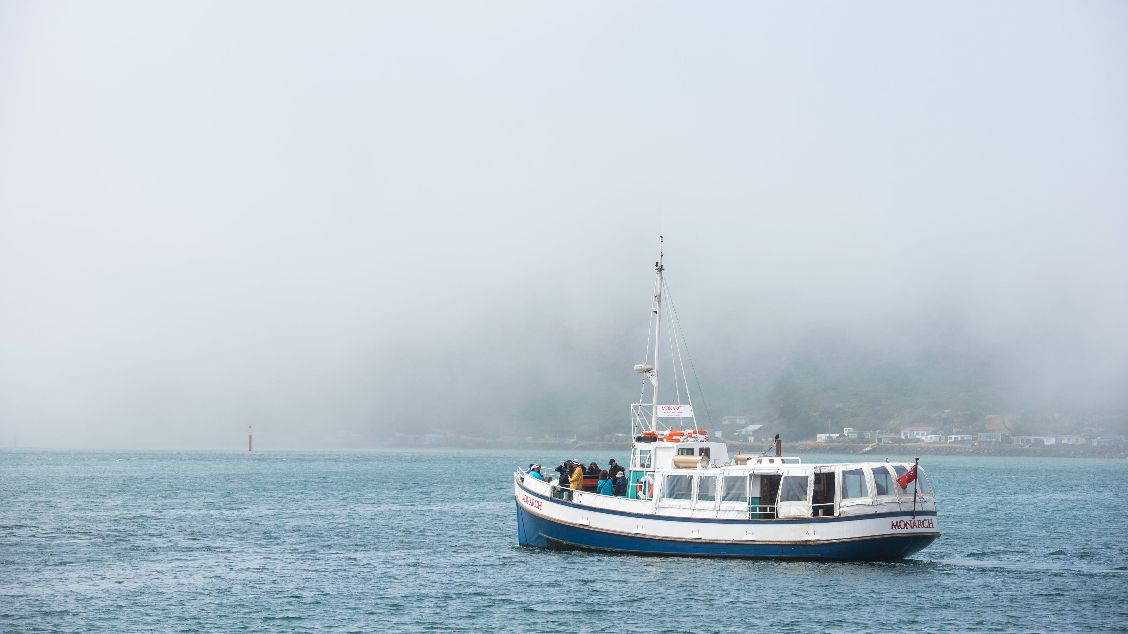 A boat named 'Monarch' on a foggy day, with a lighthouse in the distance.