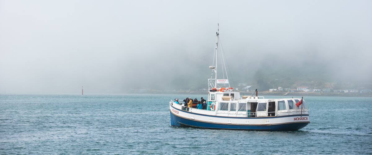 A boat named 'Monarch' on a foggy day, with a lighthouse in the distance.