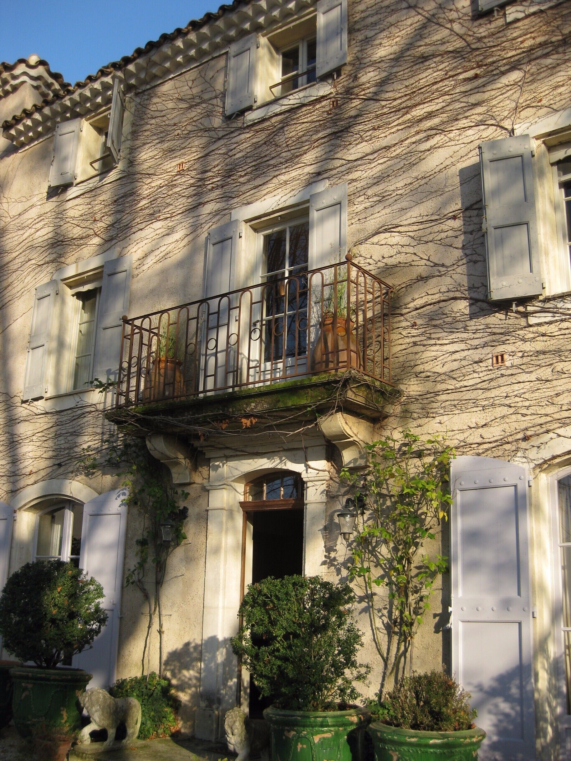 A historic stone building with a balcony, potted plants, and a door.