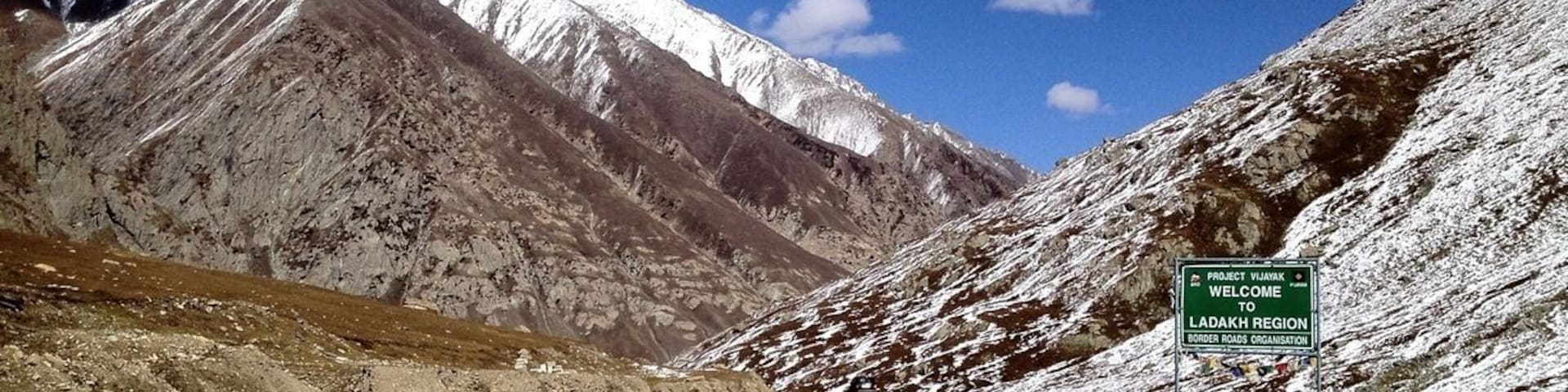 Una carretera que conduce a una cordillera nevada, con un letrero que da la bienvenida a la región de Ladakh.