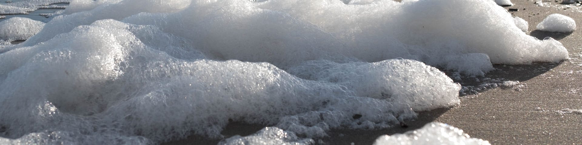 A beach with waves and foam, rocky cliffs in the background.