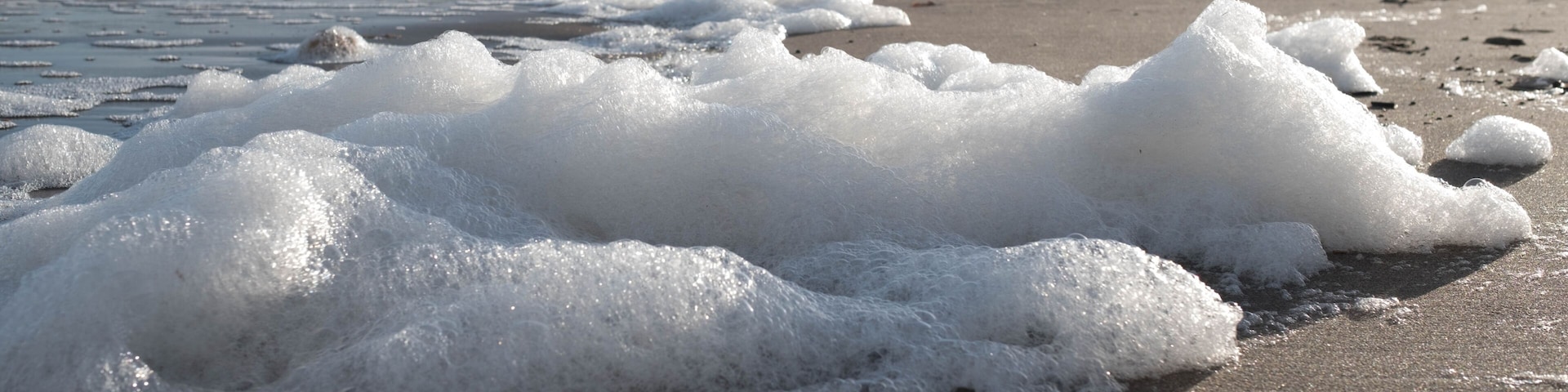 A beach with waves and foam, rocky cliffs in the background.