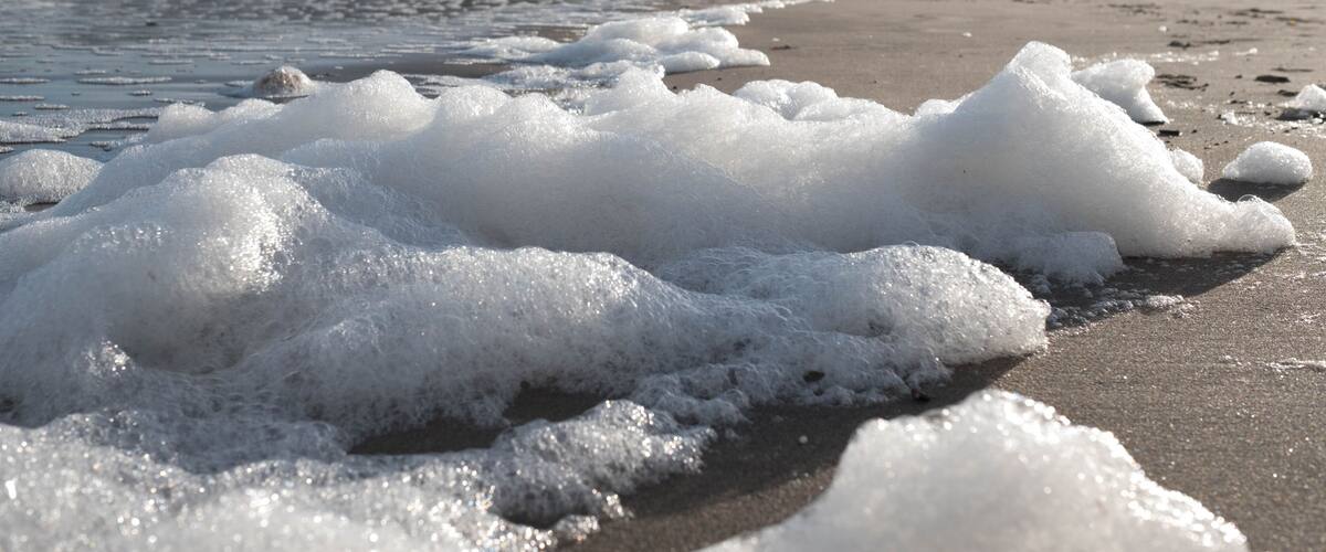 A beach with waves and foam, rocky cliffs in the background.