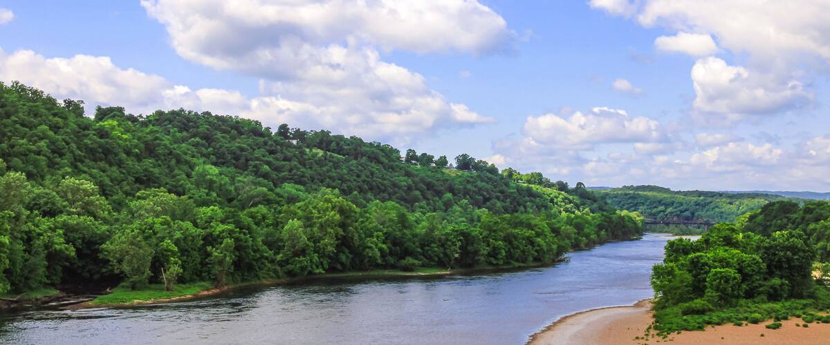 A river winding through a forested landscape with a sandy beach on one side.