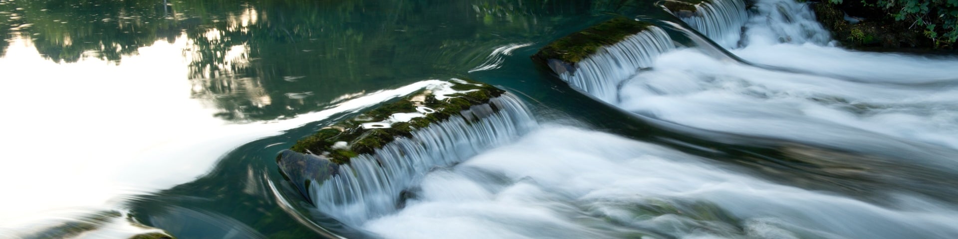 Una cascada que se precipita sobre rocas hacia un río tranquilo, rodeado de exuberante vegetación.