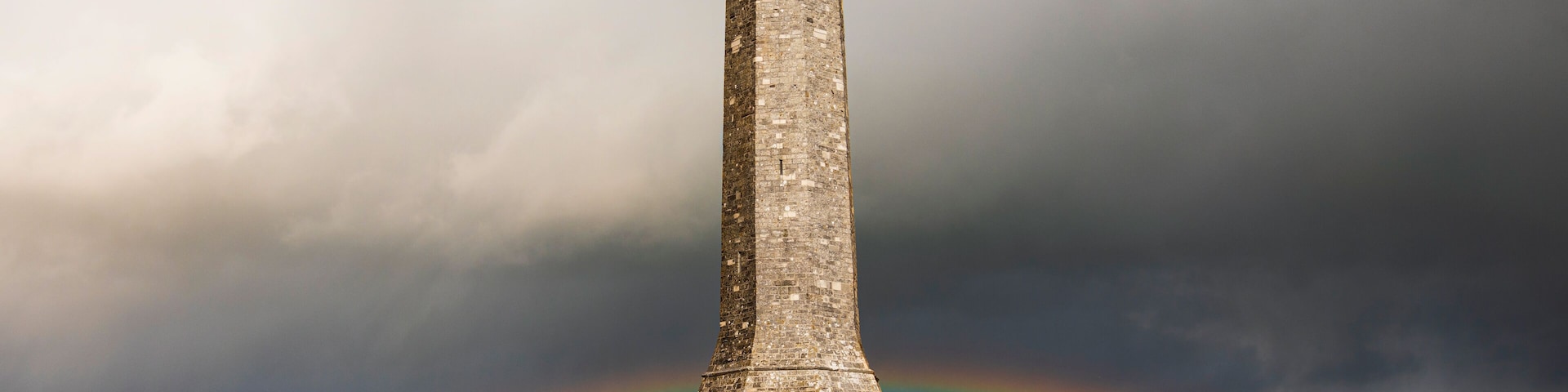 Un monumento de piedra con un arcoíris al fondo.