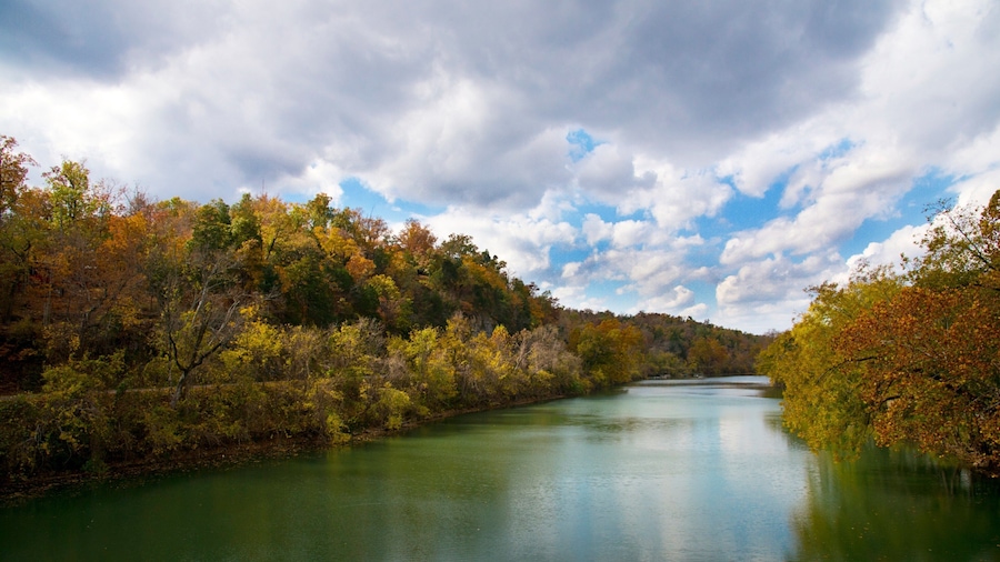 A river surrounded by autumn-colored trees under a partly cloudy sky.