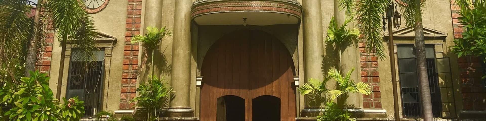 A historic church with a central dome, two statues on the facade, and a large wooden entrance.