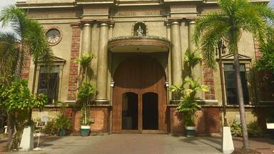 A historic church with a central dome, two statues on the facade, and a large wooden entrance.
