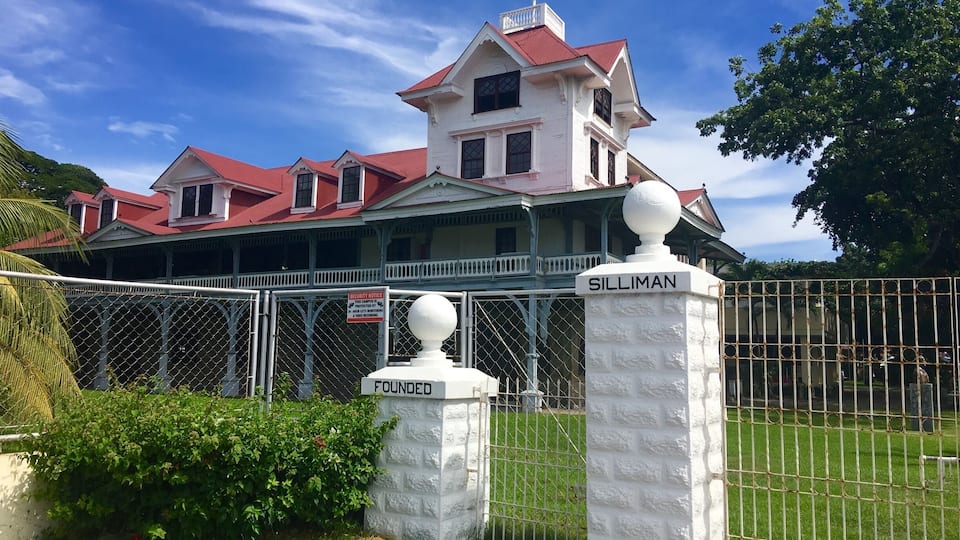 A large, white colonial-style building with a red roof, surrounded by a white fence and a sign that reads "SILLIMAN".