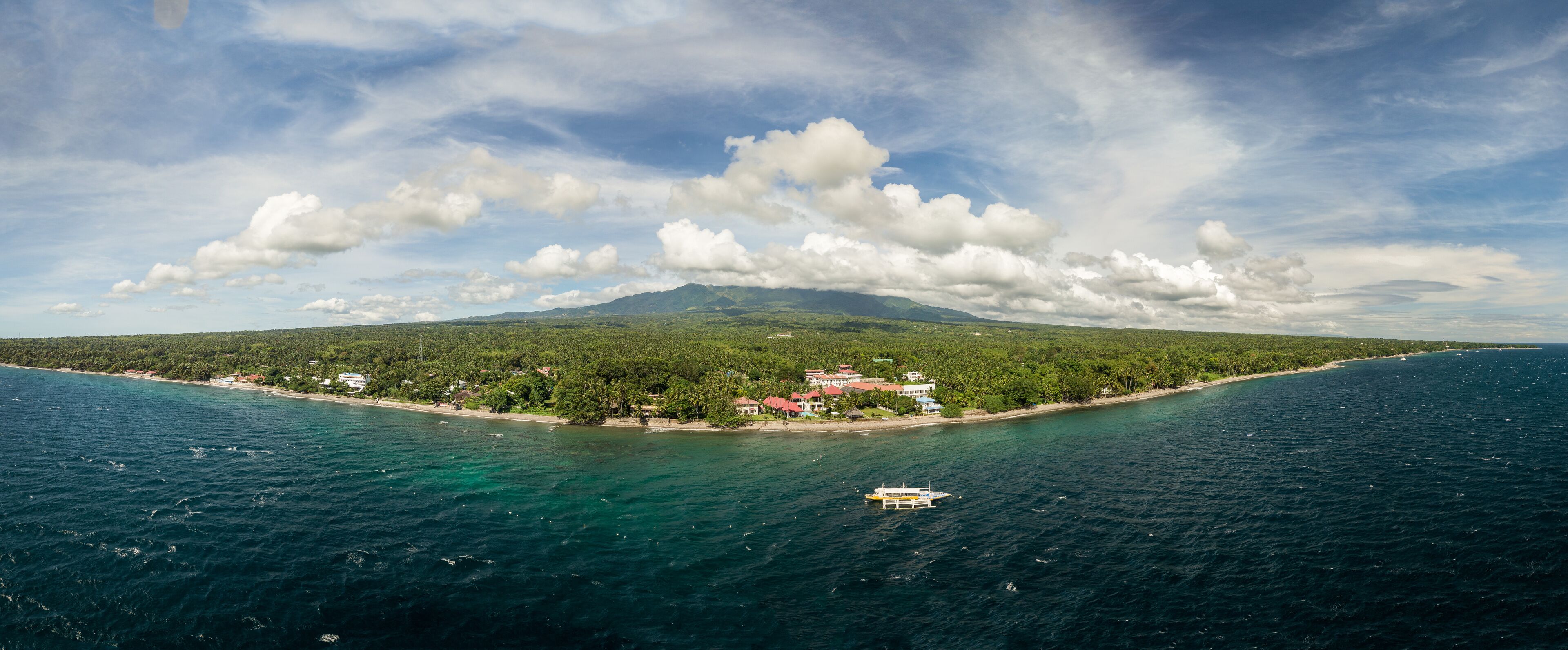 A coastal landscape with a mountain, a beach, and a boat in the water.