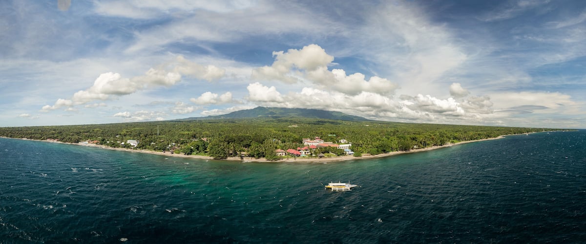 A coastal landscape with a mountain, a beach, and a boat in the water.
