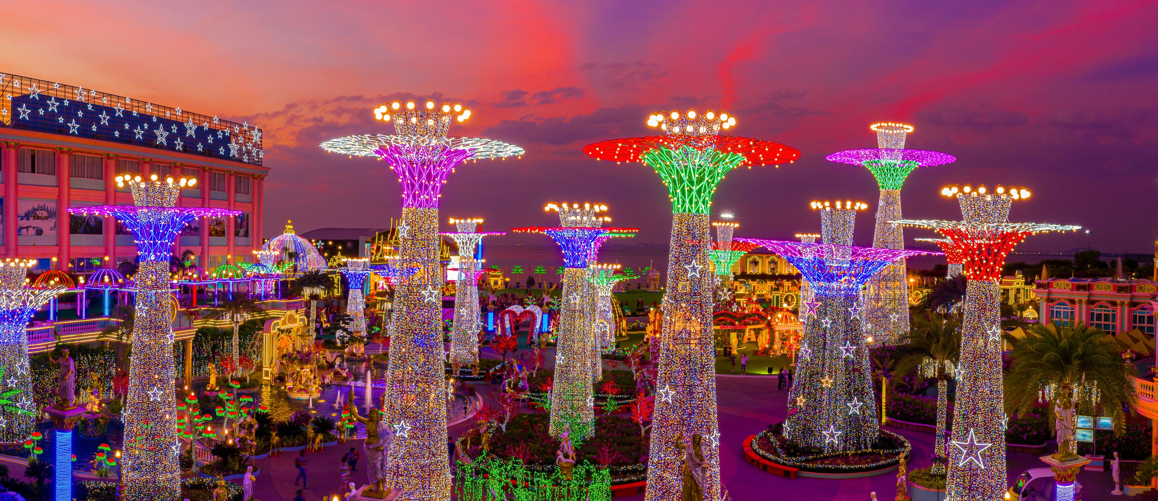A plaza with illuminated trees and statues, surrounded by buildings with star decorations.