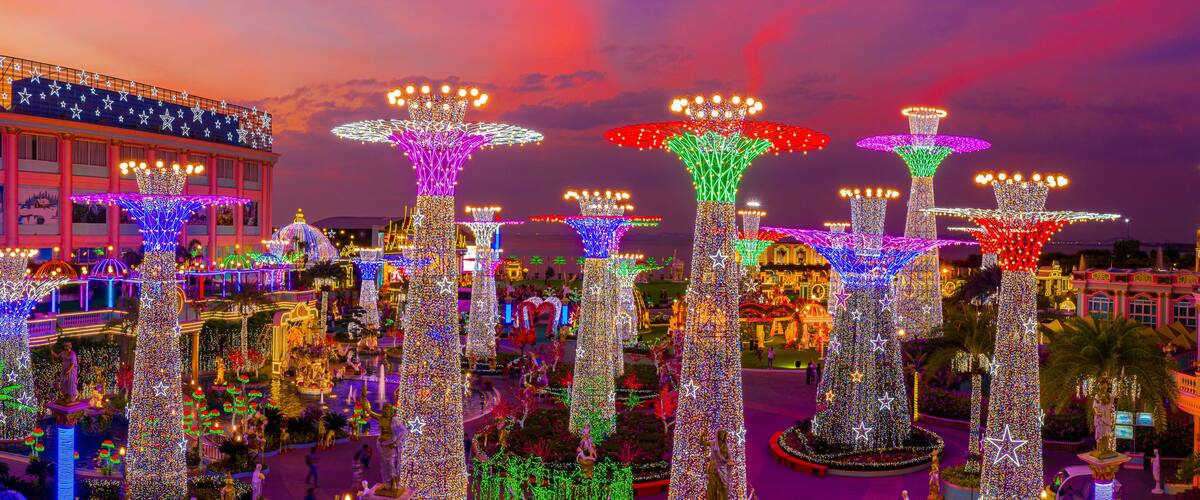A plaza with illuminated trees and statues, surrounded by buildings with star decorations.