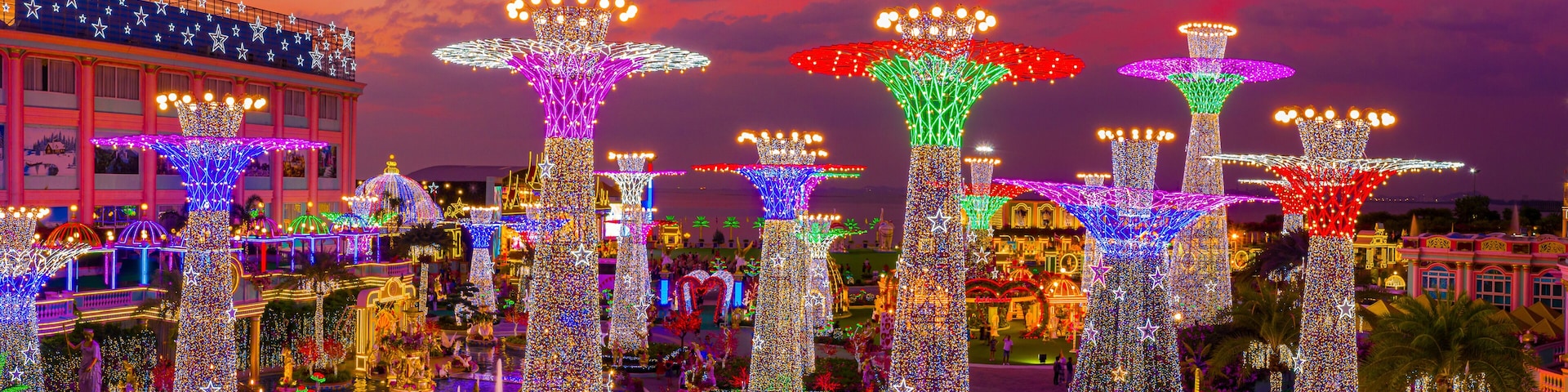 A plaza with illuminated trees and statues, surrounded by buildings with star decorations.
