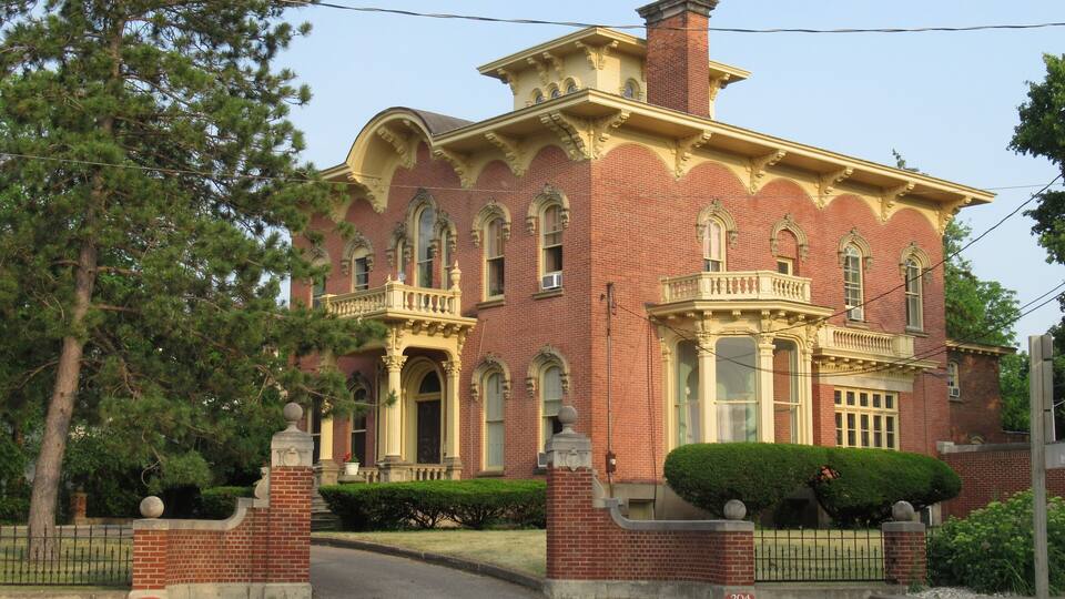 A large brick building with ornate architectural details, including a balcony and arched windows.