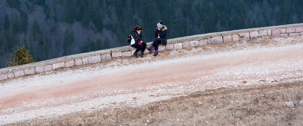 Two people sitting on a stone ledge overlooking a forested valley.