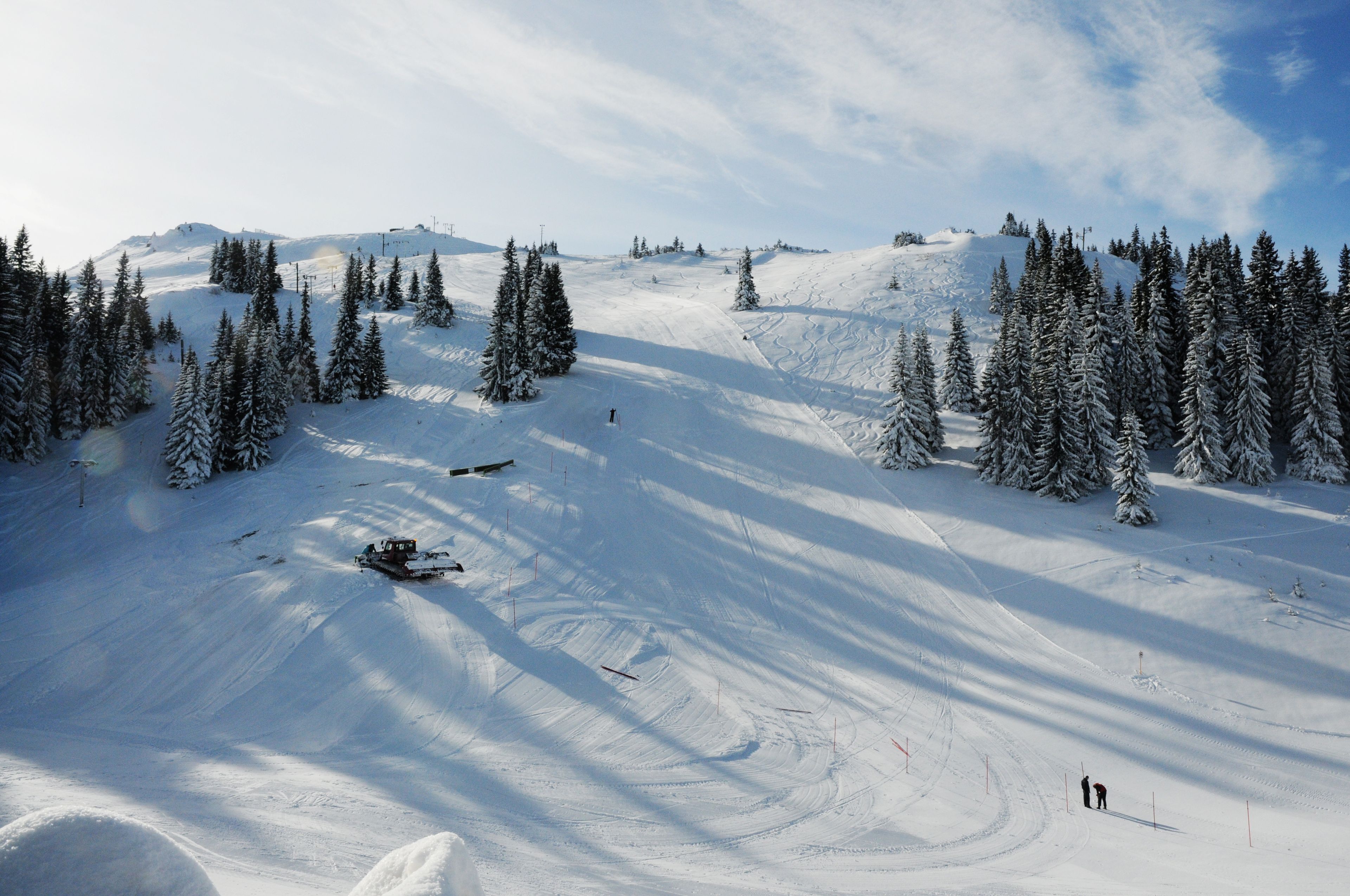 Een piste met een sneeuwdek, bomen, skiúsporen en een sneeuwscooter.