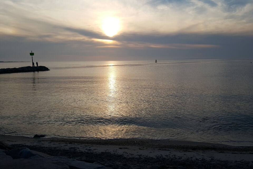 A sunset over a calm sea with a rocky shoreline and a distant buoy.