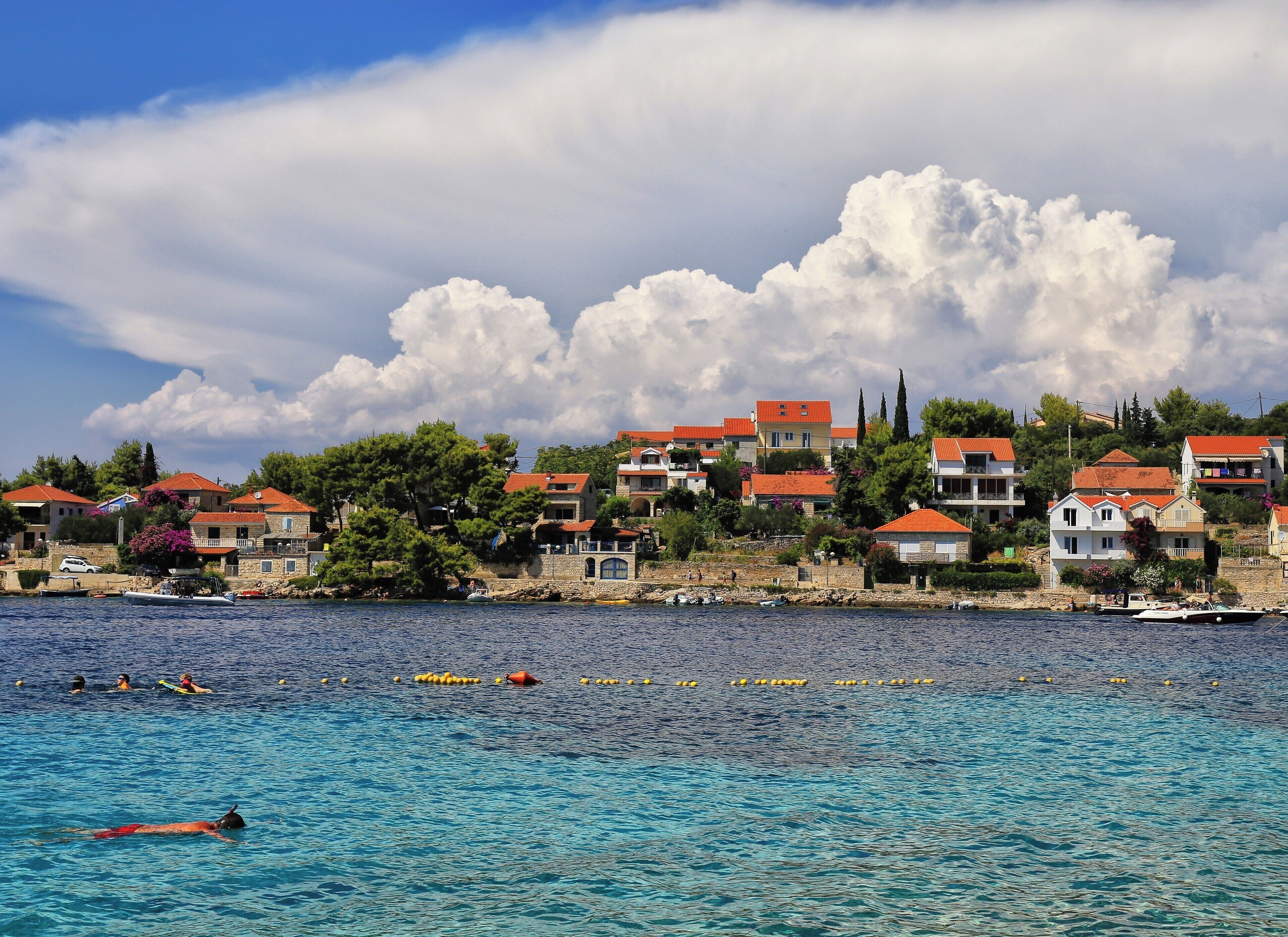 A coastal town with red-roofed buildings, clear blue water, and swimmers.