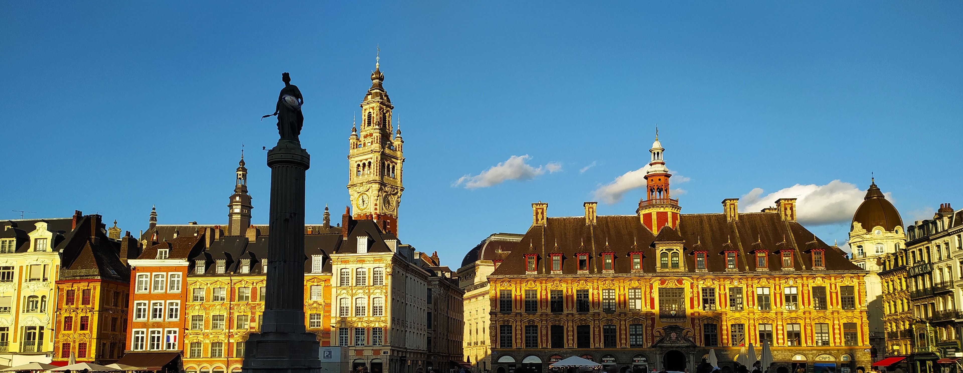 Een historisch Europees stadsplein met sierlijke gebouwen, een opvallende klokkentoren en een standbeeld.
