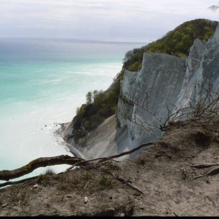 A coastal cliff with a beach and turquoise sea.
