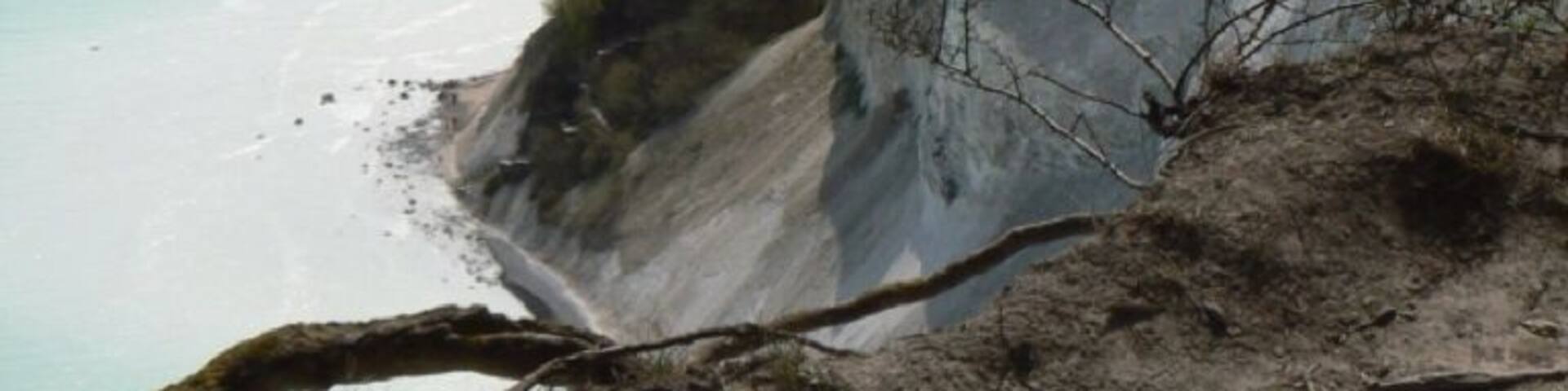 A coastal cliff with a beach and turquoise sea.