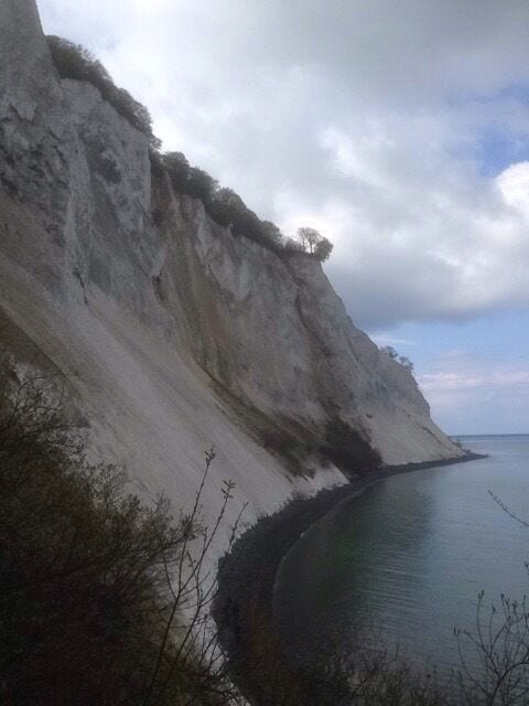 A coastal cliff with a sandy beach and a calm sea.