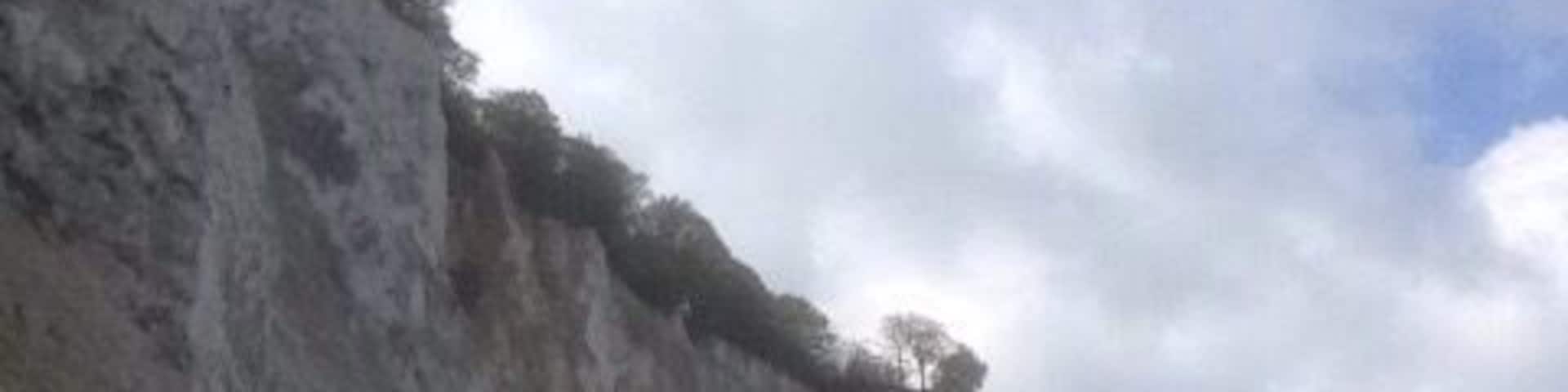 A coastal cliff with a sandy beach and a calm sea.