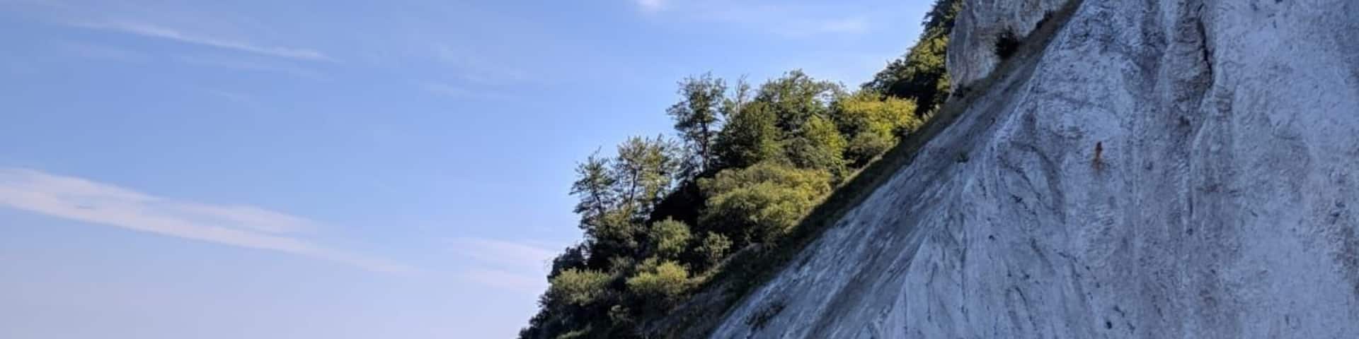 A rocky beach with a steep cliff and a clear blue sky.