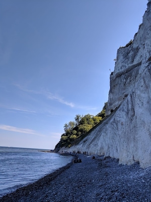 A rocky beach with a steep cliff and a clear blue sky.