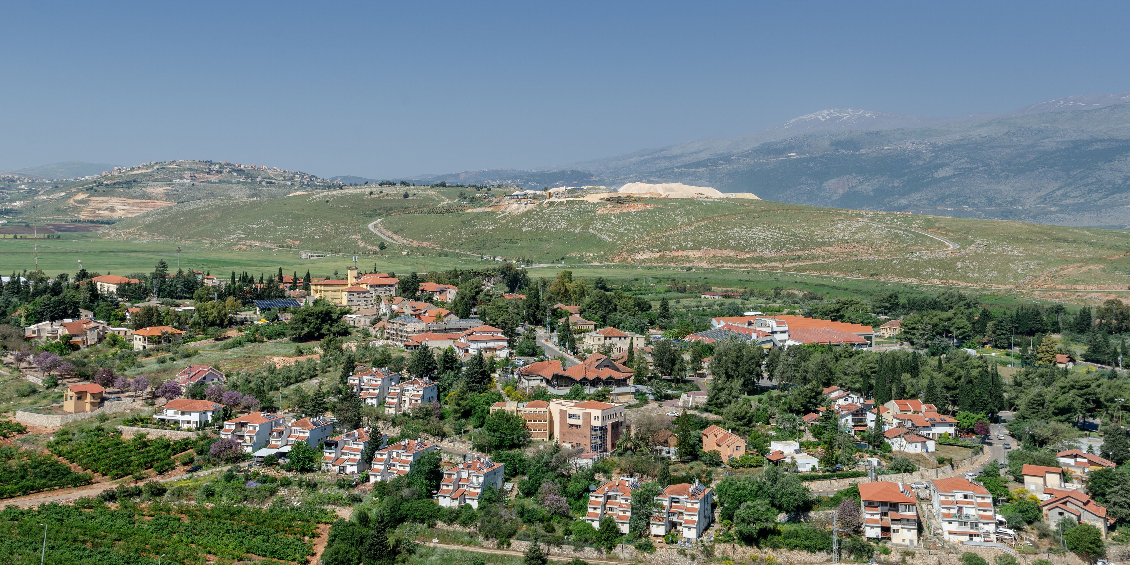 A hillside village with terraced houses, a winding road, and a distant mountain range.