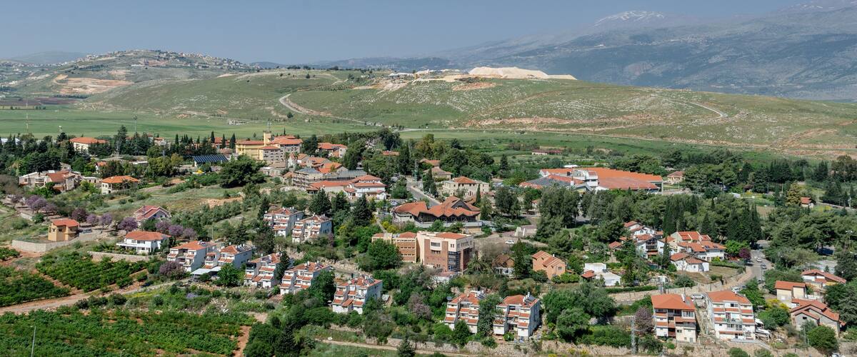 A hillside village with terraced houses, a winding road, and a distant mountain range.