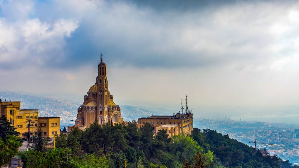 A historic church with a tall bell tower, surrounded by lush greenery and urban buildings.