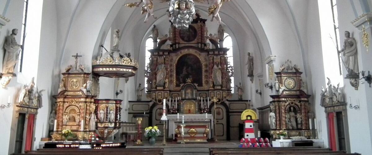 An ornate church interior with a central altar, statues, and a large crucifix.