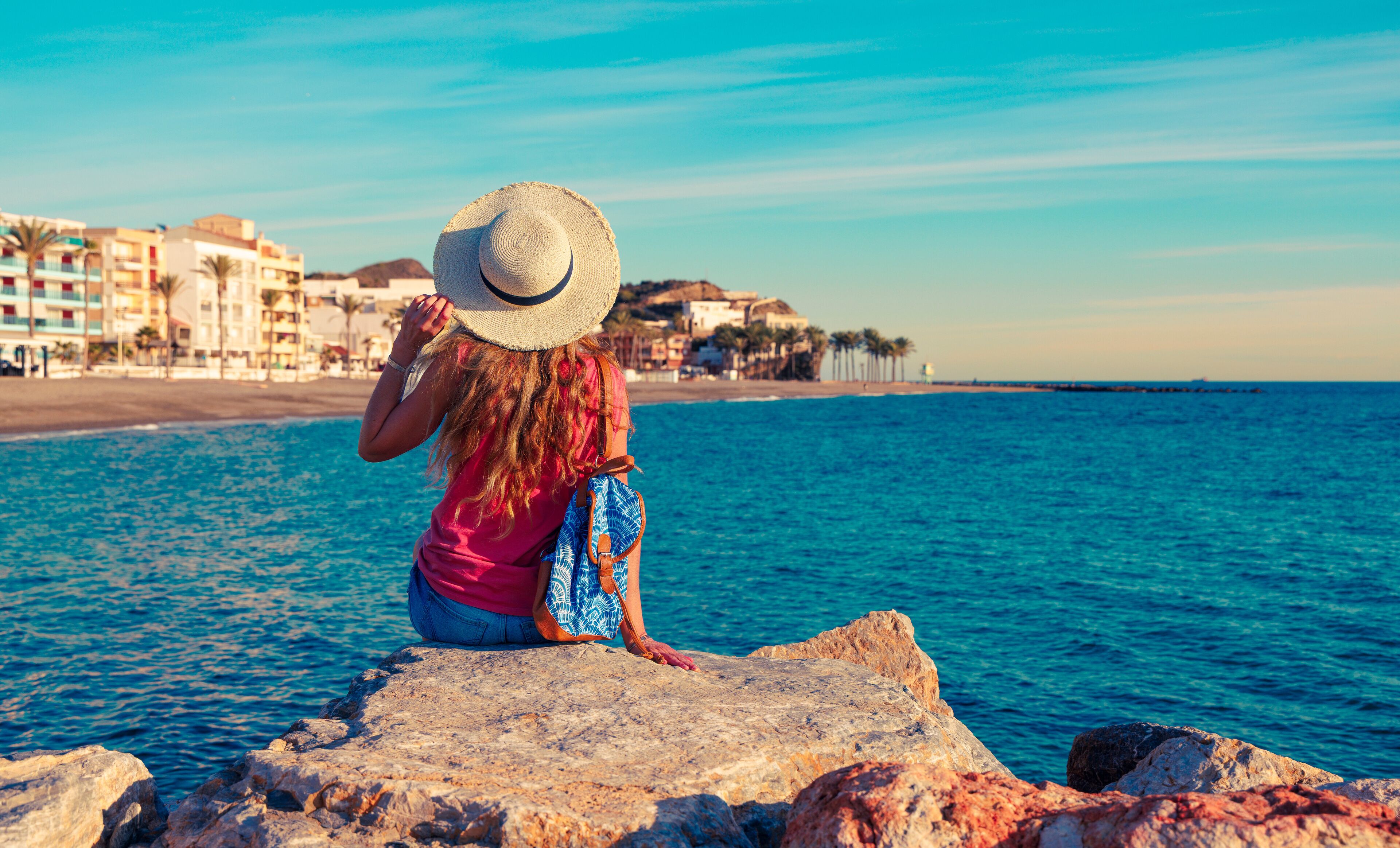 A woman sitting on rock, looking at typical village in Coasta Tropical, Andalousia, Torrenueva in province de Granada. Travel destination in Spain