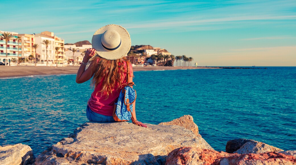 A woman sitting on rock, looking at typical village in Coasta Tropical, Andalousia, Torrenueva in province de Granada. Travel destination in Spain