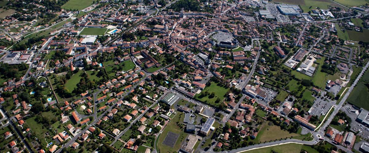 An aerial view of a town with a mix of residential and commercial buildings, surrounded by green fields and roads.